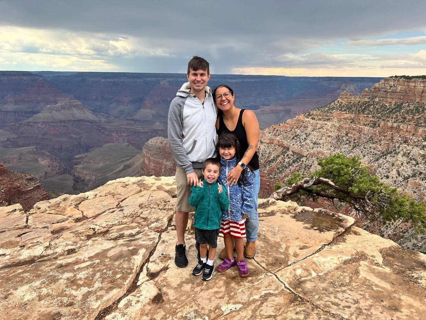 Lee Rippy with his wife and their two children standing on the rim of the Grand Canyon under an overcast sky.